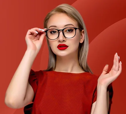 A woman with blonde hair wears glasses and bold red lipstick, set against a rich red background. She gazes confidently, touching her frames, exuding elegance.