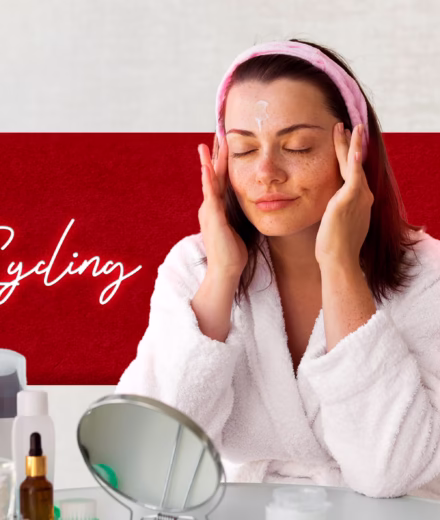 A woman in a white robe applies skincare cream to her face at a vanity with skincare products, with "Skin Cycling Routine" written in the background.